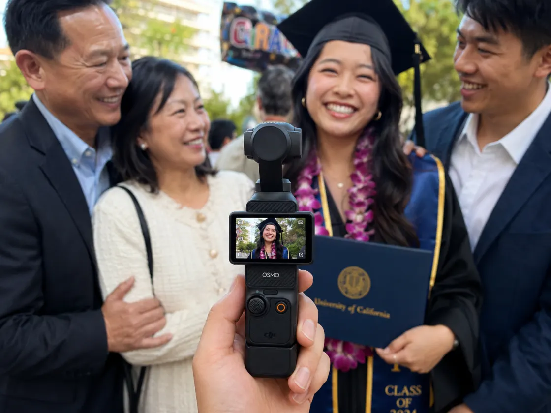 A guest filming a graduate in cap and gown with her family after the ceremony