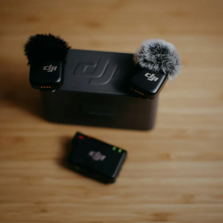 Two wireless clip-on microphones beside their charging case