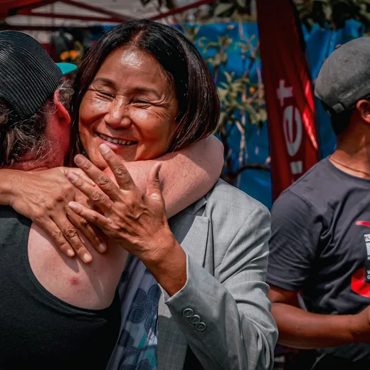 An older woman laughing as she is hugged on arrival