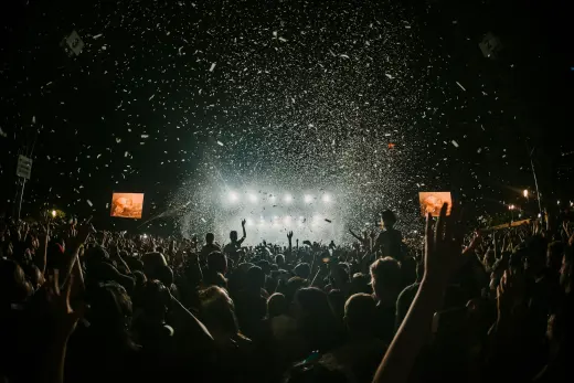 A crowd with hands up facing a lit stage as confetti falls