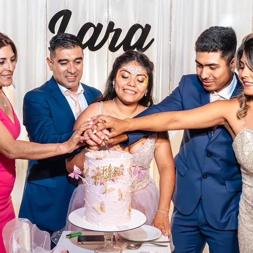 A family crowding in around a young woman to cut her birthday cake