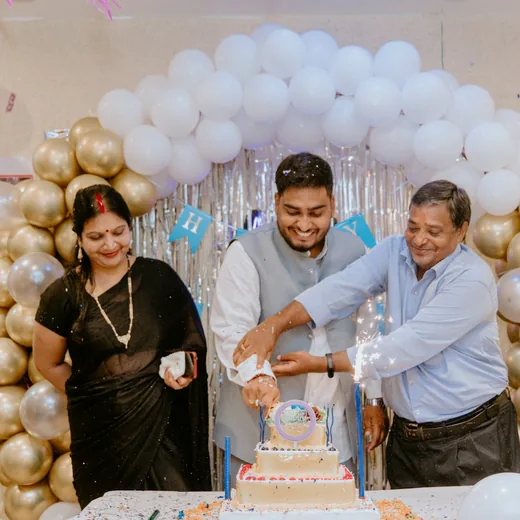 A family crowding in to cut a birthday cake under a balloon arch