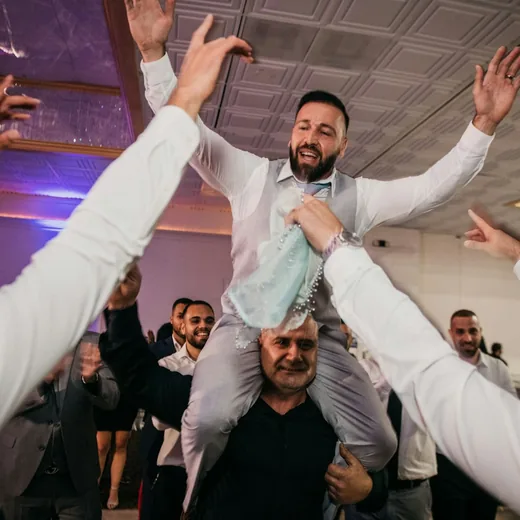 A guest carried on someone's shoulders as the room raises their hands