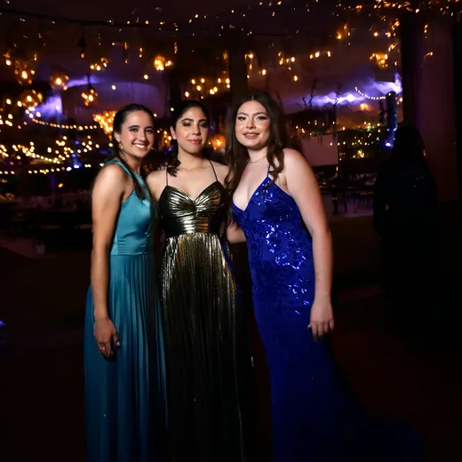 Three teenagers in gowns arriving at a party strung with lights